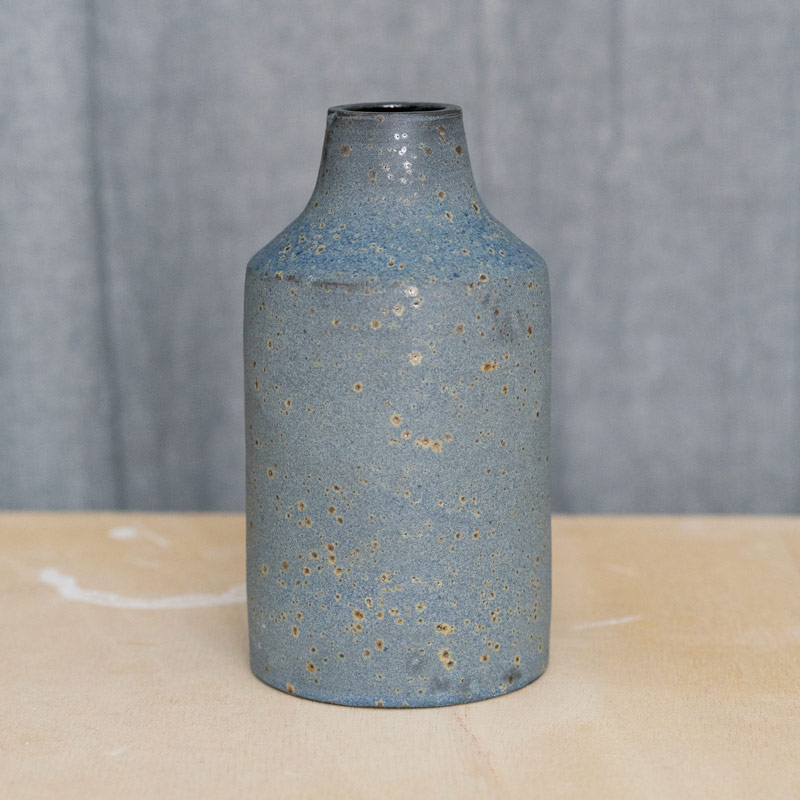 Glasurbrand Geradlinige, matte, schwarzblaue Vase vor grauem Vorhand auf Holztisch
